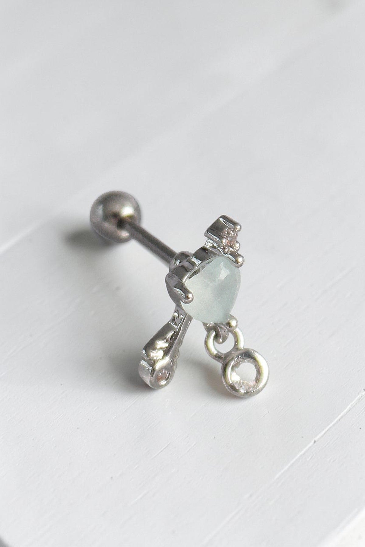 VORA HOUSE gümüş rengi paslanmaz çelik tragus piercing, beyaz mineli kalp figürlü ve zirkon taş detaylı sallantılı model